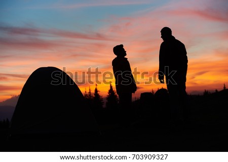 Silhouettes of a male and female tourists standing near their tent on top of a mountain stunning sunset on the background people lifestyle vitality sporty active travelling nature landscape sky.