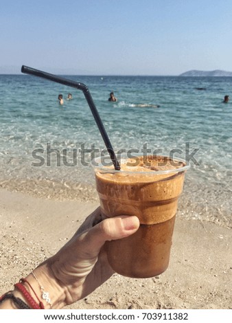 A hand holding a frappe against sea in Greece