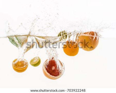 Cut fruits are thrown into the water in transparent vessel. Orange, lime, grapefruit and water splash on white background.