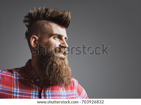 Young trendy man portrait. Punk styled man with Mohawk hairstyle is smiling. Isolated on gray background