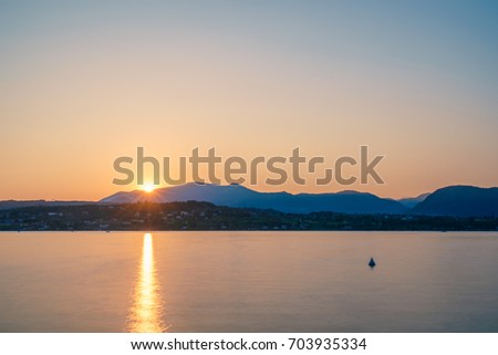 Sunset behind a mountain range at Lake Garda as along exposure with a reflection of the sun, Itlay