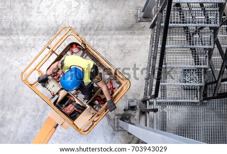 Aerial of a worker with blue hardhat on a cherry picker Royalty-Free Stock Photo #703943029