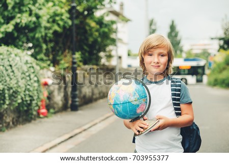 Outdoor portrait of funny little kid boy wearing backpack and holding world globe. Back to school concept. Film look filter image