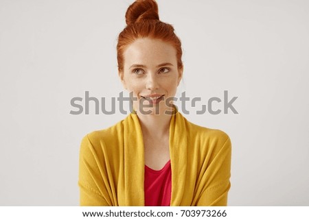 Daydreaming, ideas, thoughts and anticipation concept. Picture of cute teenage girl wearing her ginger har in bun looking up and biting her lips while dreaming about something pleasant and nice