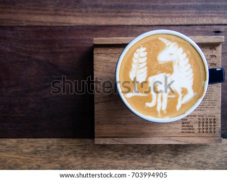 Cup of coffee with beautiful unicorn and tree shape latte art foam on wooden background with copy space. Top view.