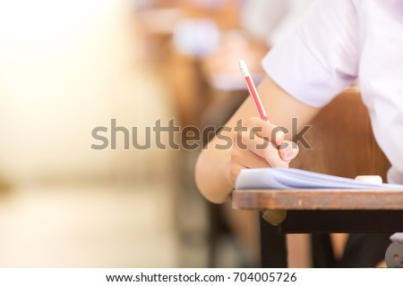 soft focus.high school or university student holding pencil writing on paper answer sheet.sitting on lecture chair doing final exam attending in examination room or classroom.student in uniform. Royalty-Free Stock Photo #704005726
