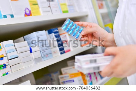 Pharmacist holding medicine box and capsule pack in pharmacy drugstore. Royalty-Free Stock Photo #704036482