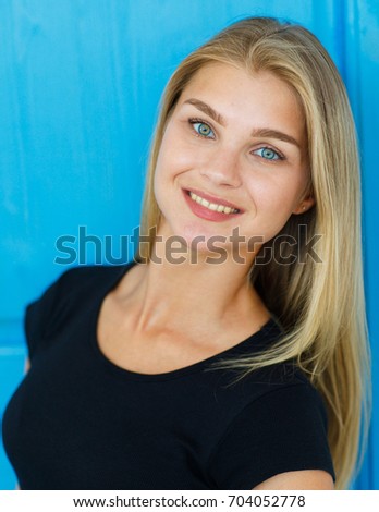 Joy, fun and happiness concept. Horizontal portrait  of a positive smiling girl with blond hair in a black T-shirt on a blue wooden door background. People, lifestyle, leisure and relaxation
