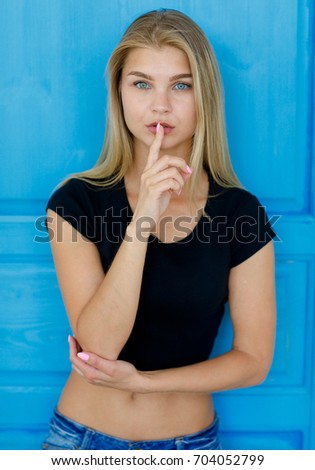 Keep silence!  Close up Indoor shot of beautiful female  in black T-shirtwith finger on lips on a blue door background. People, youth, leisure and lifestyle concept.
