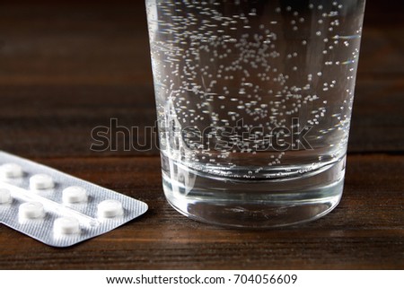 The tablets lie next to a glass of water on the table. Disease, flu, cold. Treatment, medicine.