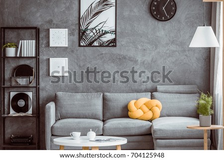 Yellow knot pillow on grey settee in living room with coffee table and black shelf with mirror