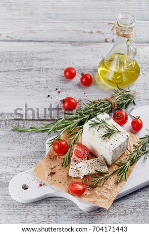Fresh feta cheese with cherry tomatoes and rosemary on white wooden serving board over light wooden background