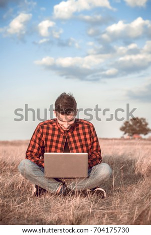 Happy man using his laptop compiuter and sitting on the field