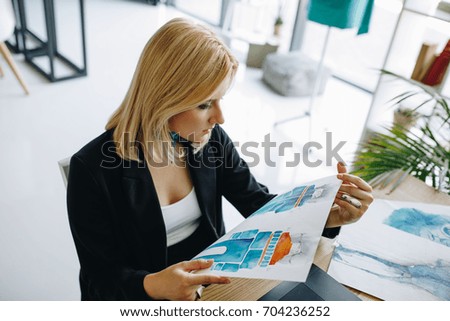 beautiful young female fashion designer holding sketch while sitting at workplace