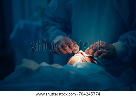 Surgeon and his assistant performing cosmetic surgery on nose in hospital operating room. Nose reshaping, augmentation. Rhinoplasty. Royalty-Free Stock Photo #704245774