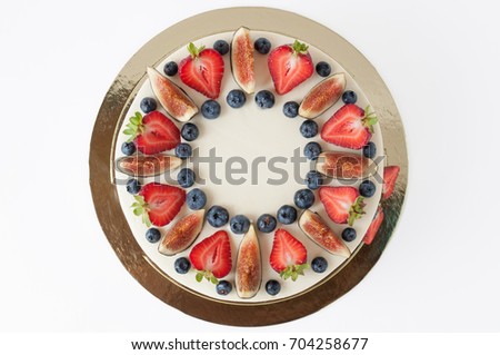 Cake with whipped white cream, decorated with fresh strawberries, blueberries and figs. Picture for a menu or a confectionery catalog. Isolated. Top view.