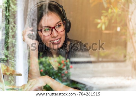 Pretty asia woman wearing headphones  Listen to relaxing music Happily, by this picture, the view through the glass. Reflected from the garden Beautifully decorated