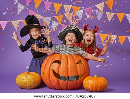 Happy brother and two sisters at Halloween. Funny kids in carnival costumes on background of purple wall. Cheerful children and pumpkins with confetti.