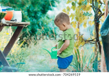 The little boy in the village at sunset in the summer with a watering can sprinkler
