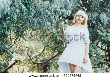 Charming blonde girl on a background of green trees at sunset