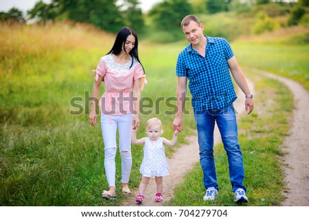 happy family walks in the park, baby holding her parents by the hand