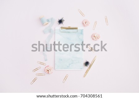 Flat lay of clipboard, rose buds, blue ribbon, golden pen and clips on pale pink background. Top view stylish decorated mock up.