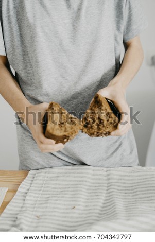A young woman holds a homemade hand-made bread with sunflower seeds. breaks the bread in half.