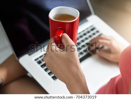 Red coffee cup in woman hand relax with using laptop at the morning