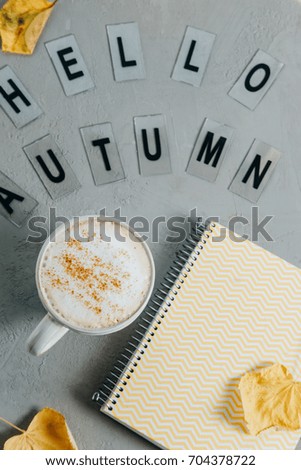 Workspace with notebook, cup of coffee, leaves and words "Hello autumn". Top view, flat lay