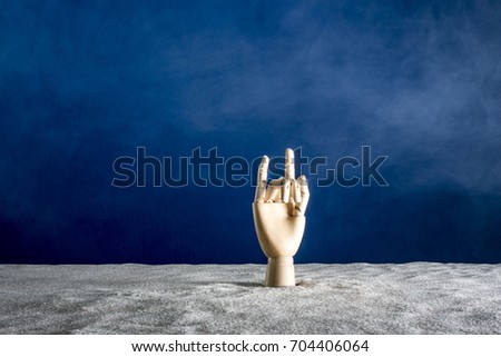 Wooden hand gesticulating against a white sand and blue sky background