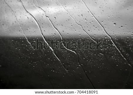Raindrops flow over the glass. Bad weather, the last day of summer, the gray sky. View from the window of the car. Horizon, landscape, nature.
