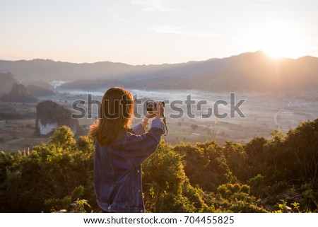 Young woman taking photos of sunrise in mountain at Phu Lung ka,Thailand