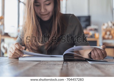 Closeup image of a beautiful Asian woman reading a book in modern cafe 