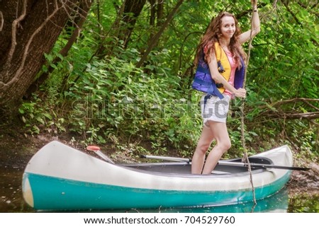 Cute girl holding lianas standing in a kayak on a stream in the forest in a life jacket