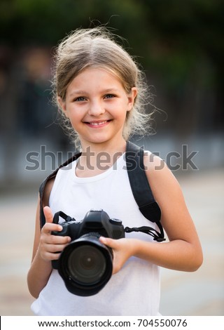 portrait of smiling girl in elementary school age holding photo camera in summer day