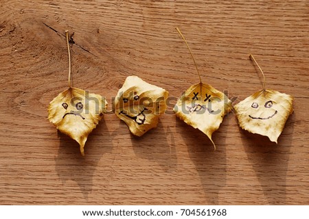 Yellow leaf with a picture of a sad face on the old wooden background with cracks