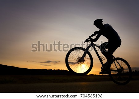 Silhouette of boy on the bike. Young cyclist is jumping on his bike during sunset. Fore wheel is over the horizon. Royalty-Free Stock Photo #704565196