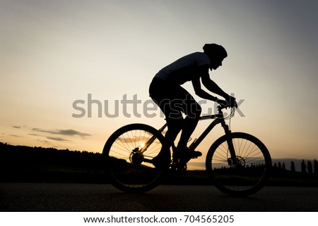 Silhouette of boy on the bike. Young cyclist is riding his bike during sunset. Royalty-Free Stock Photo #704565205