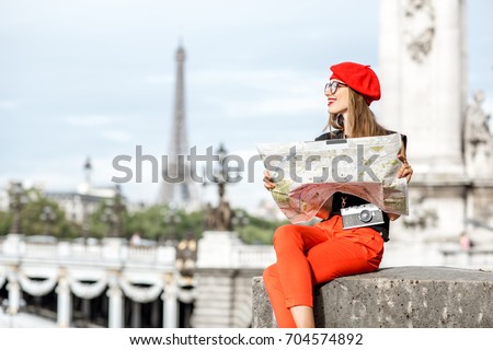 Young woman in red holding a tourist map sitting on the footbridge with Eiffel tower on the background in Paris