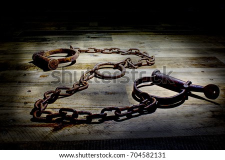Old fashioned, vintage shackles on a rustic wooden background. The picture is reflective of incarceration, jail, kink, bound, rust, corrosion, cuffs, vintage, law enforcement, antiques Royalty-Free Stock Photo #704582131