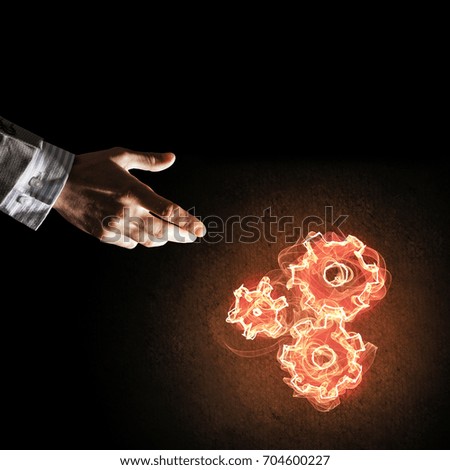 Hand of businessman pointing fire gear mechanism on dark background