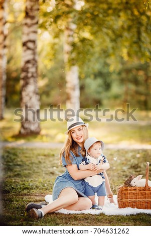 Ideal family: mother and baby son sitting in park on grass playing with rabbits. Concept childhood