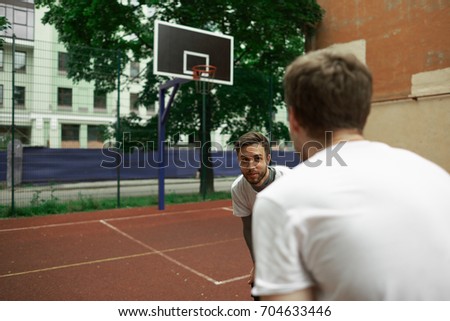 People, leisure, entertaining, hobby, sports and healthy lifestyle. Outdoor summer portrait of handsome smiling bearded man with dark hair playing streetball game with his unrecognizable friend