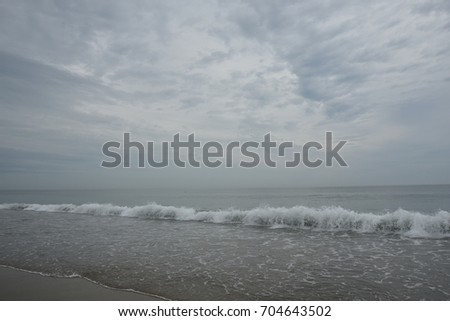 The angle of a breaking wave bisects the picture plane under a sky of rippled clouds.