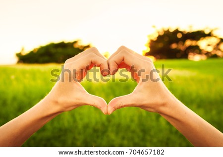 Love, people, nature, adventure. Hand shaped heart in a grass field. 