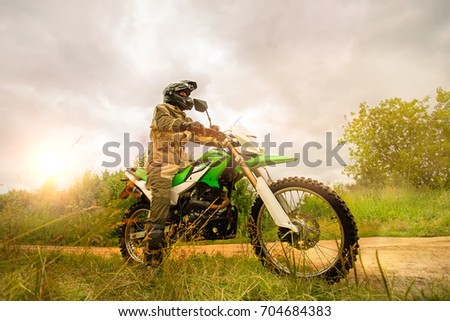 Man wearing motorcycle helmet and safety uniform sitting on a dirt bike outdoors, beautiful scenic landscape on the background in daytime setting. Motorcross concept.