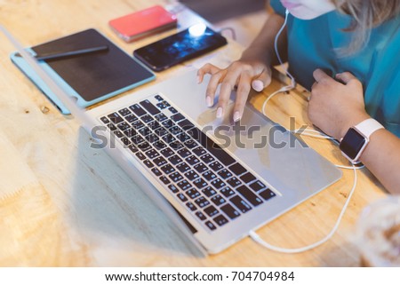 Close up Asian woman wearing pink smartwatch and working with her laptop in coffee shop in selective focus.