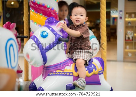 Happy little baby boy  riding carousel horse