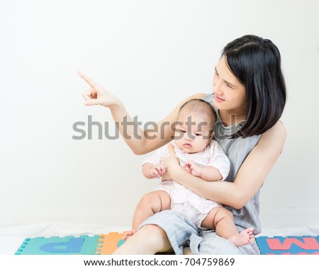 Portrait of happy asian mother hugging her cute baby and pointed the finger to left side