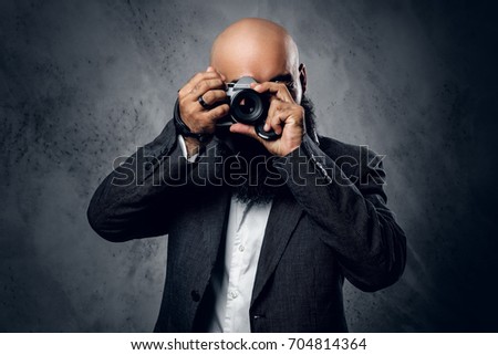 Elegant bearded professional photographer in a suit shooting with a compact DSLR camera.